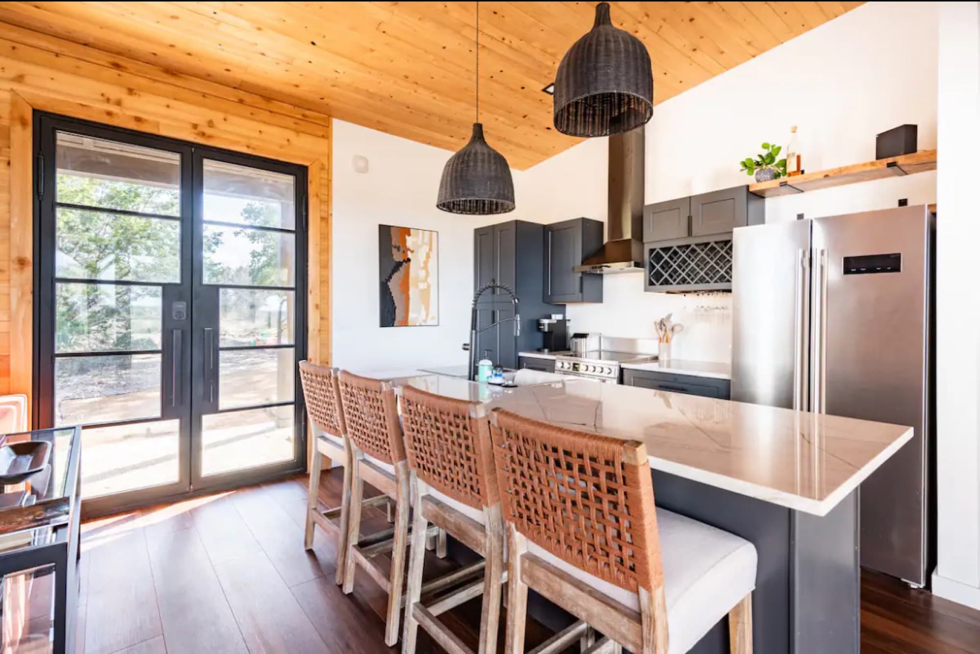 The cabin kitchen with an island, woven stools and steel doors to the porch