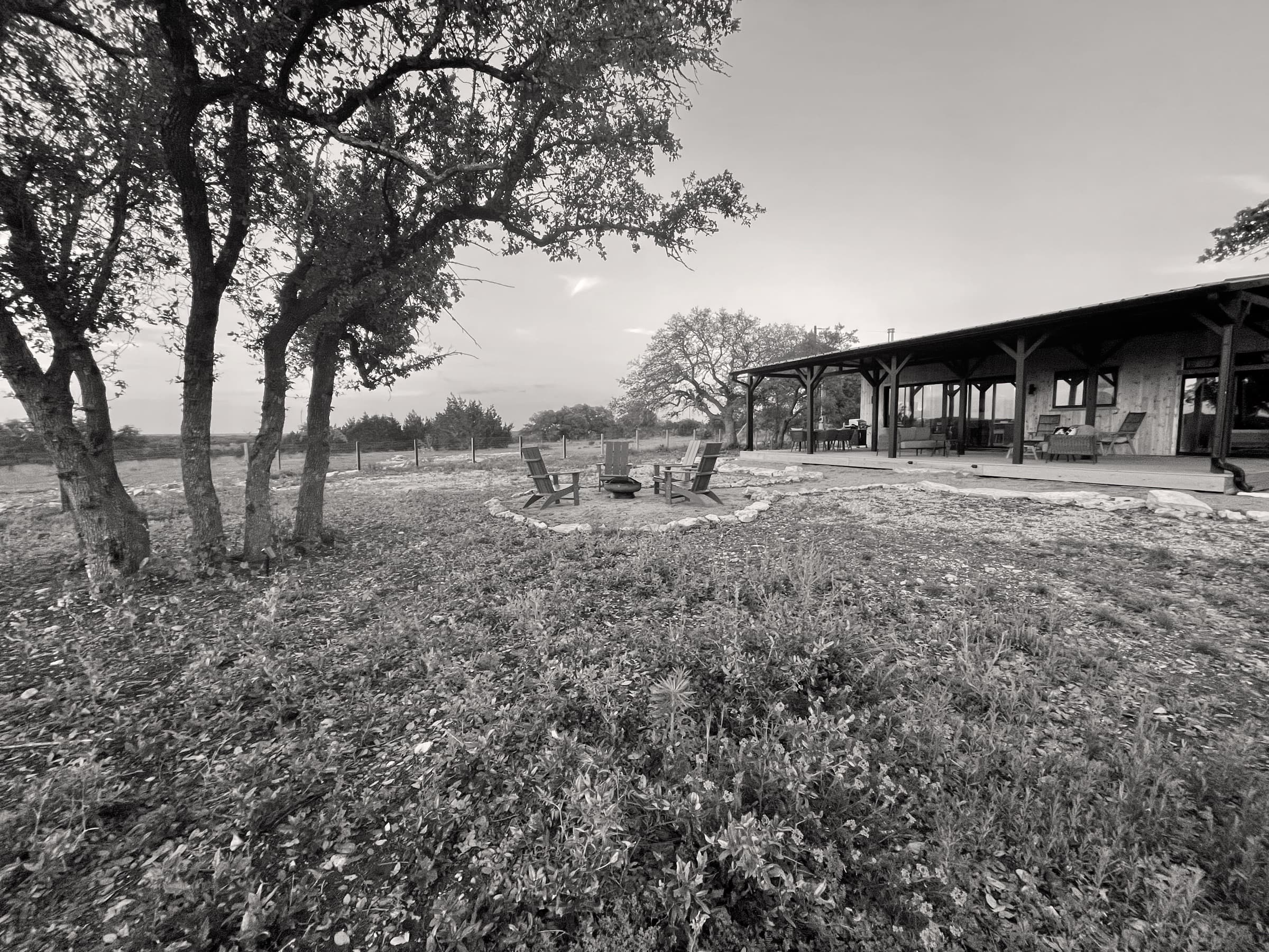 The cabin at Lazy Dog Ranch at dusk: the firepit with four chairs under the live oaks, the long covered porch behind